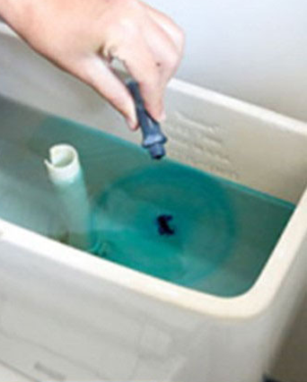 Person adding a drop of a blue water leak detector into an open toilet tank to test for leaks