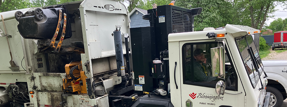 A person using a garbage truck with an arm to lift a garbage cart and dump it into the garbage truck