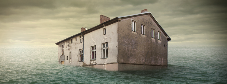 Large house that appears to be sitting in a large body of water with dark clouds overhead.